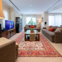 Real estate photography of a living room with sectional sofa, entertainment unit, and Persian rug