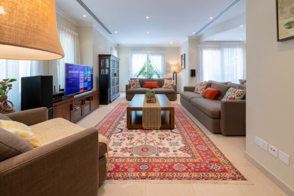 Real estate photography of a living room with sectional sofa, entertainment unit, and Persian rug