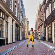 Destination photographer Amsterdam — traveller leaping along a quiet canal street with bicycles