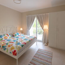 Real estate photography of a bright bedroom with floral bedding, side tables, and curtained window
