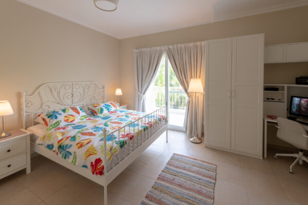 Real estate photography of a bright bedroom with floral bedding, side tables, and curtained window