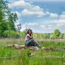 Environmental portrait of woman seated on fallen log in grassland, Hoge Veluwe National Park