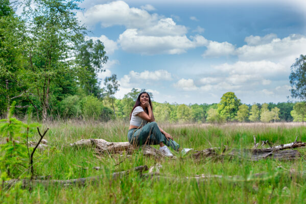 Environmental portrait of woman seated on a fallen log in grassland, Hoge Veluwe National Park