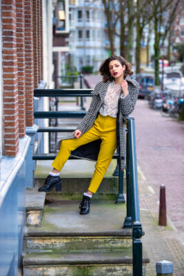 Travel portrait of woman in yellow trousers on classic Amsterdam canal-house doorsteps — visiting traveller shoot
