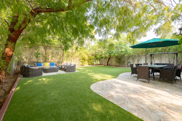 Real estate photography of a private back garden with green lawn, mature trees, patio furniture, and parasol