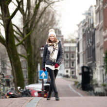 Street portrait of blonde woman in a dark coat with a white scarf on a canal street, Amsterdam Centrum