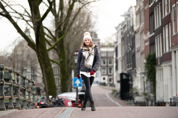 Street portrait of blonde woman in dark coat with white scarf on a canal street in Amsterdam Centrum
