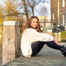 Sunlit fashion portrait of woman in cream sweater seated on a wooden post near Westerpark