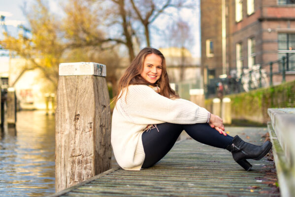 Sunlit portrait of woman in cream sweater on a wooden post at the Westerpark waterfront, Amsterdam
