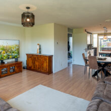 Real estate photography of a styled living room with vintage sideboard, plants, and dining area beyond