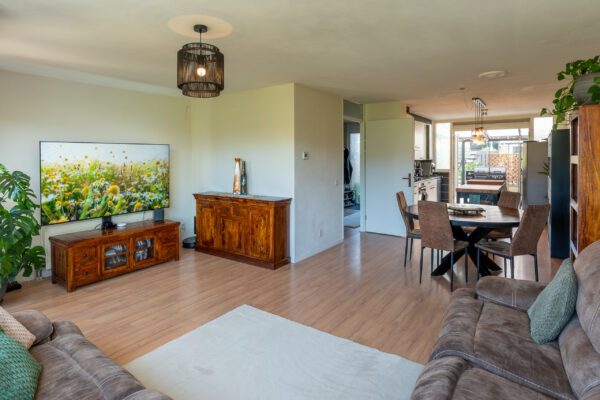 Real estate photography of a styled living room with vintage sideboard, plants, and dining area beyond