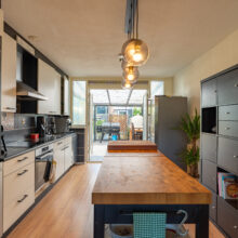 Real estate photography of a modern dark kitchen with pendant lighting and adjoining dining area
