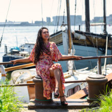 Industrial-chic portrait of woman in floral dress seated on a moored boat at NDSM Wharf, Amsterdam Noord