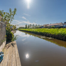 Real estate photography of a residential canal with green banks, dock, and quiet waterway