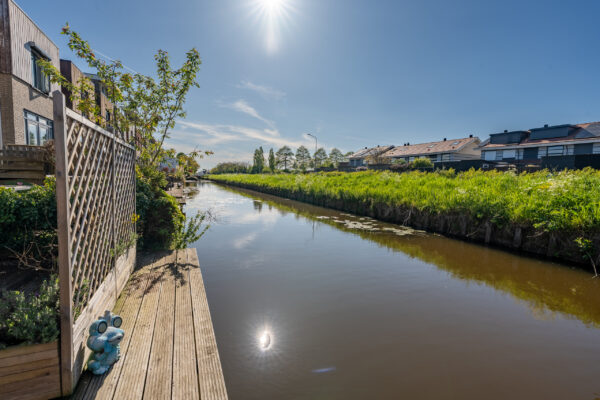 Real estate photography of a residential canal with green banks, dock, and quiet waterway