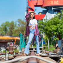 Portrait of woman in patterned dress and wide-brimmed hat among shipyard cargo at NDSM
