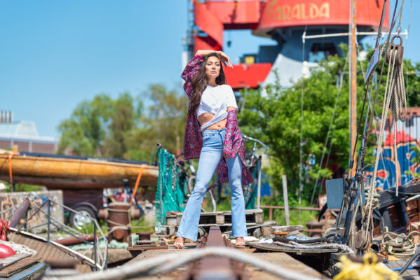 Editorial fashion portrait of woman in patterned dress and wide-brimmed hat among shipyard cargo at NDSM