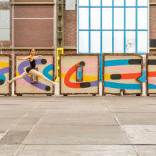 allet dancer in mid-leap in front of the colourful "Noord" sign inside an NDSM warehouse, Amsterdam Noord