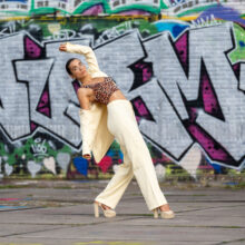 Urban portrait of woman in patterned top and white trousers in front of NDSM graffiti wall