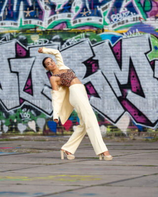 Urban portrait of woman in patterned top and white trousers in front of NDSM graffiti wall