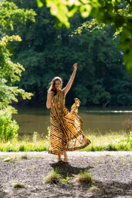Forest portrait of woman in patterned dress with arms raised in Amsterdamse Bos, Amsterdam