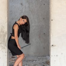 Fashion model standing against the wall at a construction site in Amsterdam, wearing red heels, black skirt and top.