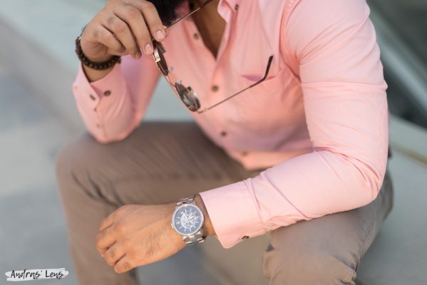 Photograph of the upper body only of a fashion model in Amsterdam wearing a pink shirt, watch while holding a pair of sunglasses.