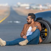 Fashion blogger and model photographed sitting on the road leaning against the front wheel of a powerful Mustang GT sports car in Amsterdam.