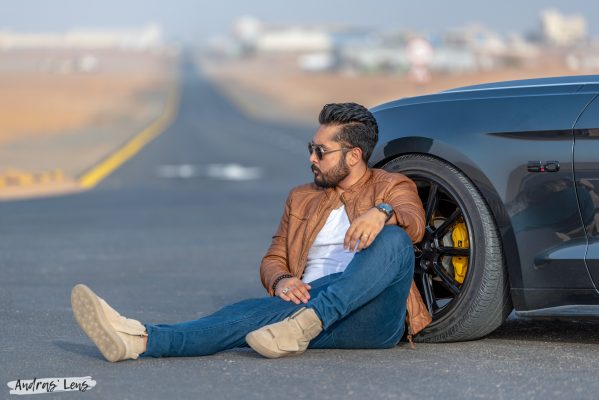 Fashion blogger and model photographed sitting on the road leaning against the front wheel of a powerful Mustang GT sports car in Dubai.