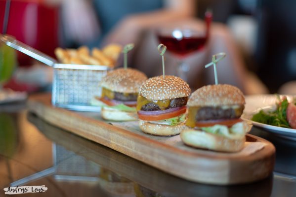 3 mini burgers photographed with fries in the background.