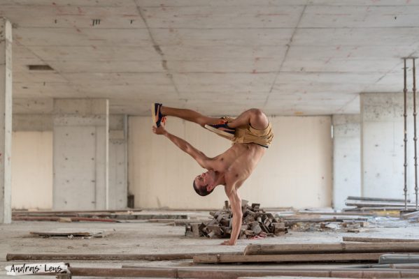 Professional one-hand stand instructor poses during a lifestyle photoshoot in Amsterdam, doing a one-hand stand and holding one of his feet in the air with the other hand.