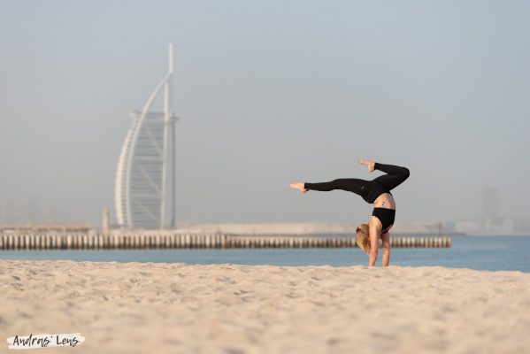 Lifestyle photography shoot for professional athlete performing a difficult handstand on the beach in Amsterdam with her feet pointing towards the Burj Al Arab.