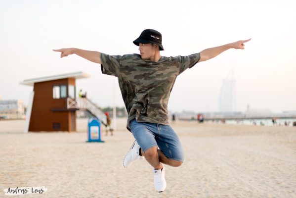 Photo of a hip hop dancer jumping in the air on a beach in Dubai with the Burj Al Arab in the background.