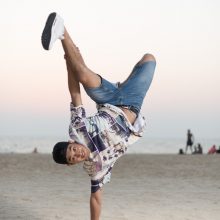 Portrait photo of a young man performing one-hand stand on a beach in Amsterdam.