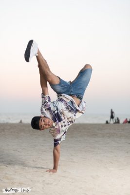 Portrait photo of a young man performing one-hand stand on a beach in Amsterdam.