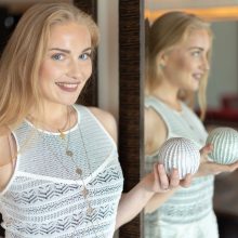 Photo of a smiling woman standing by the mirror looking into the camera while holding a round decoration in her left hand in a hotel in Amsterdam.