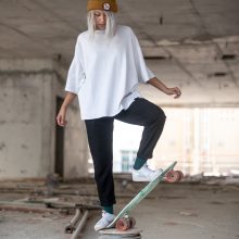 Portrait of a young girl balances on a skateboard wearing black pants, white T-shirt and a brown hat.