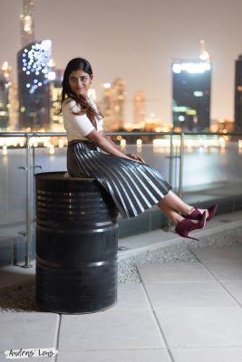 Photo of a girl in A fashionably-dress woman in a skirt smiling as she sits on top of barrel in Dubai.