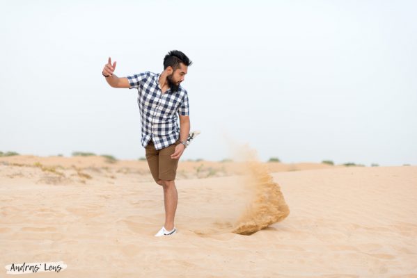 Photo of a young man playfully kicking sand backwards in the deserts of Dubai.